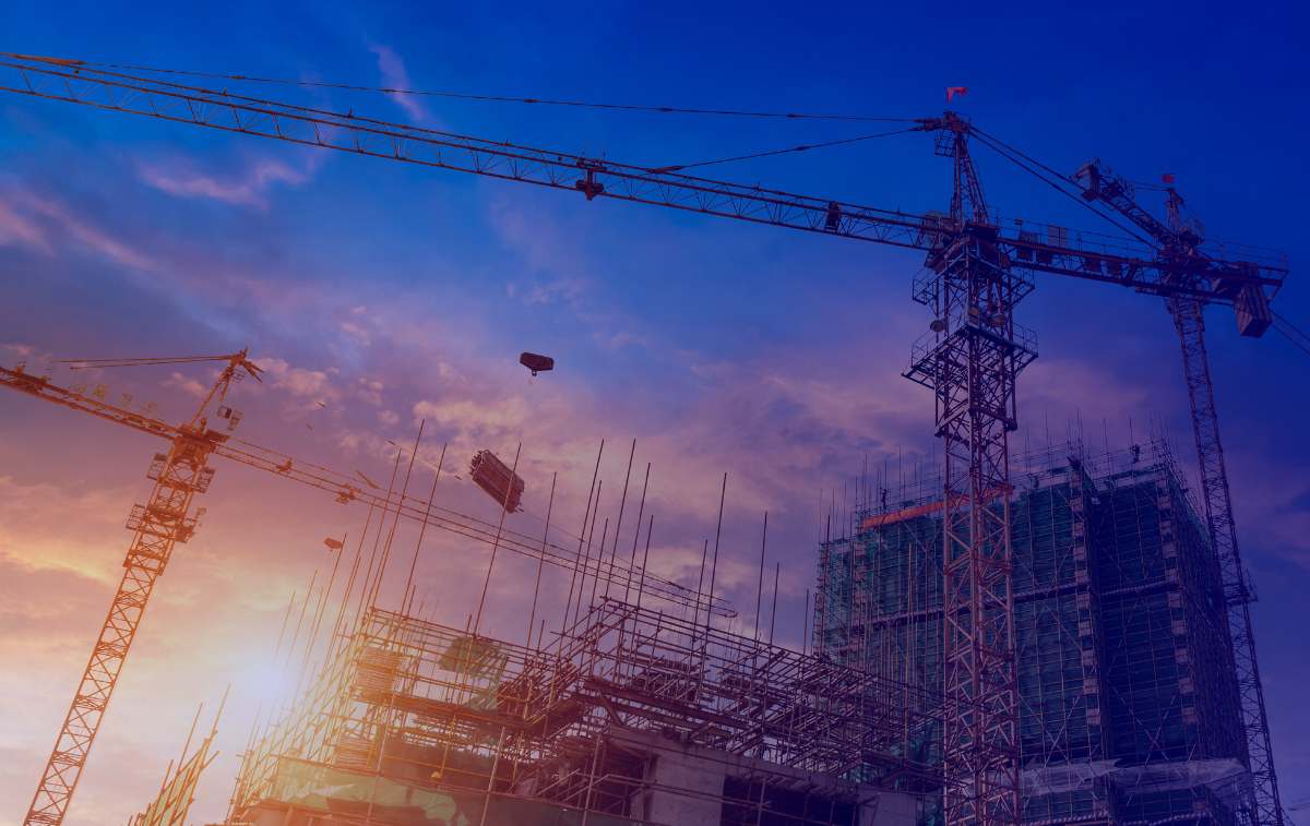 A construction site at sunset with cranes and scaffolding, symbolizing the connection between construction employment and apartment prices.