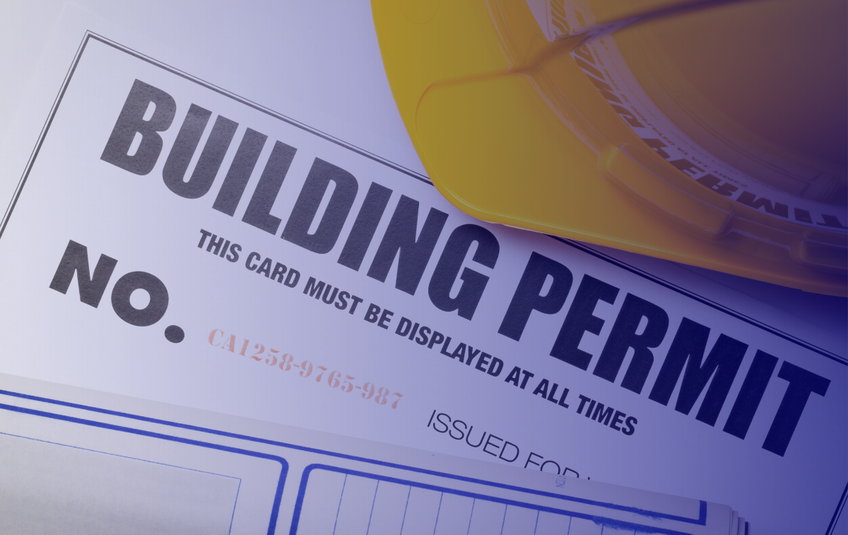 Building permit for multifamily housing units with a yellow hard hat in the background, representing the construction industry's regulatory process.